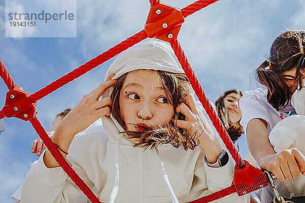 Teenager-Mädchen mit Kapuze spielt im Klettergerüst auf dem Spielplatz