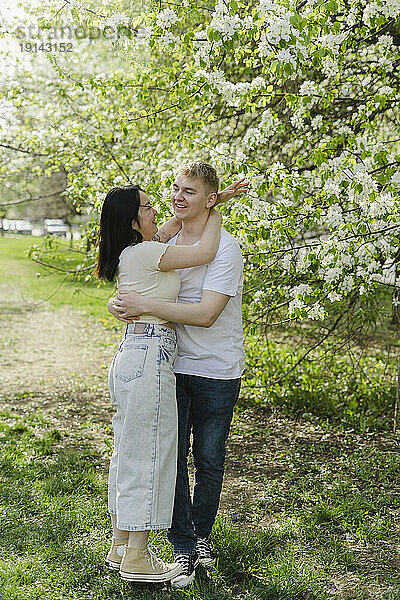 Junges Paar umarmt sich neben einem blühenden Baum im Park