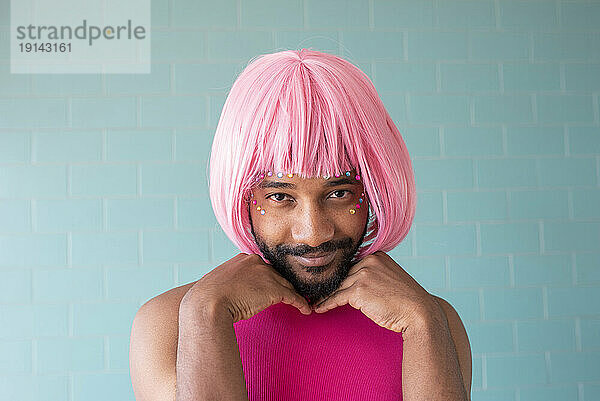 Young queer man wearing pink wig in front of tiled wall