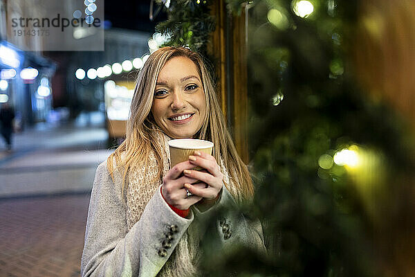Glückliche junge Frau mit Kaffeetasse auf dem Weihnachtsmarkt