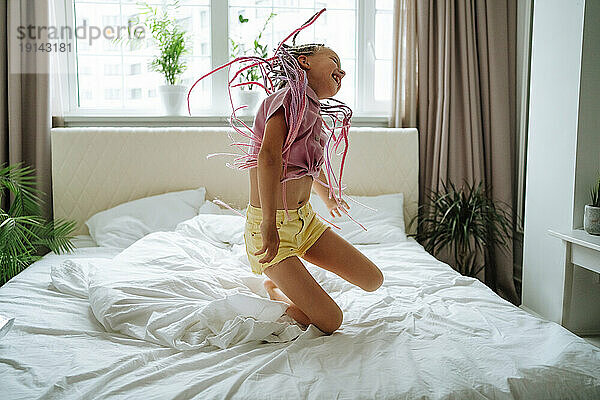 Fröhliches Mädchen mit rosa Dreadlocks  das auf dem Bett springt