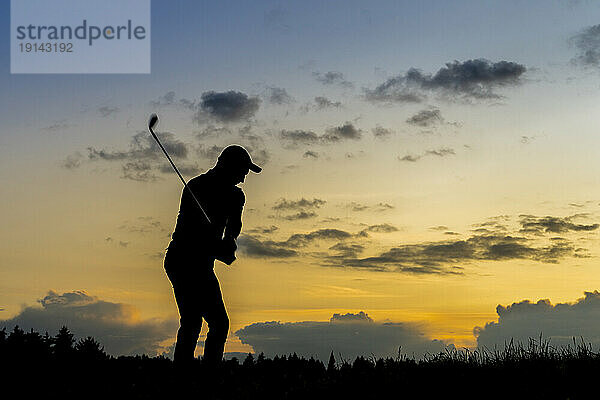 Silhouette eines Mannes  der in der Abenddämmerung Golf spielt