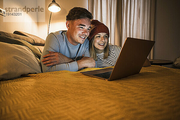 Glückliche Frau und Mann  die zu Hause einen Laptop auf dem Sofa benutzen