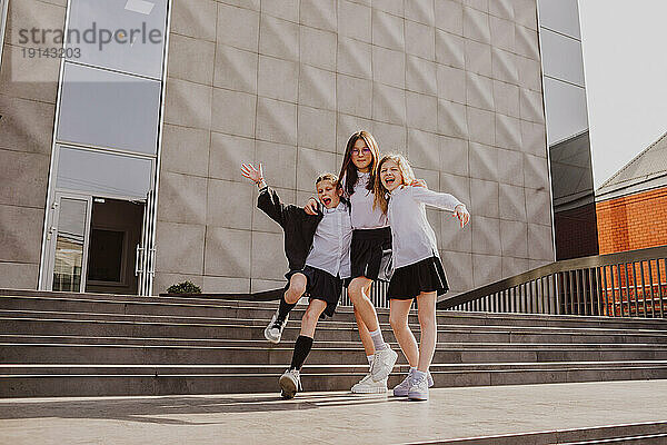 Happy schoolgirls enjoying near stairs standing in front of school building