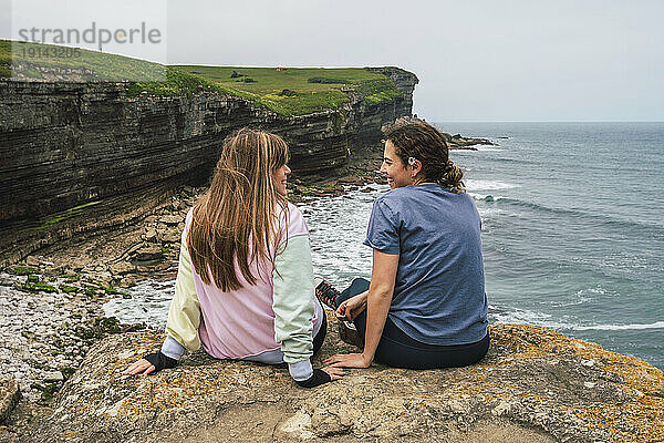 Junge Freunde reden miteinander und sitzen auf einem Felsen am Strand