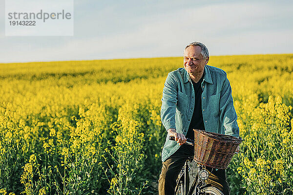 Lächelnder älterer Mann fährt Fahrrad im Rapsfeld