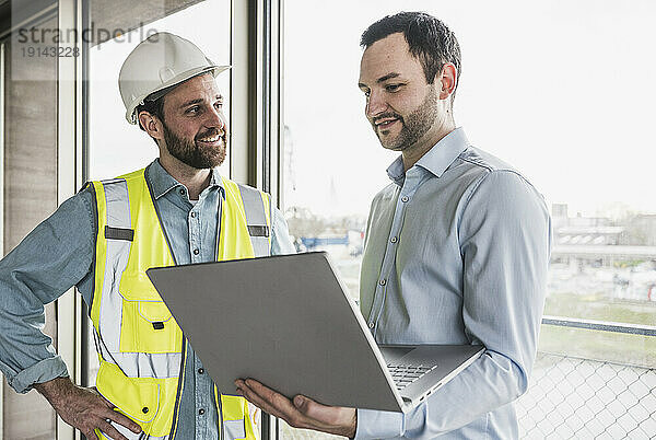 Lächelnder Bauunternehmer  der den Architekten mit Laptop ansieht