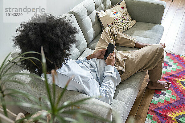 Mann benutzt Smartphone und entspannt sich zu Hause auf dem Sofa
