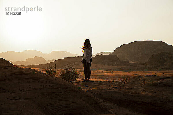 Junge Frau steht bei Sonnenuntergang in der Wüste