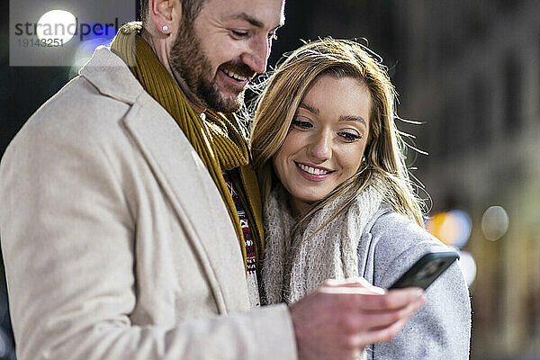 Lächelnder Mann und Frau  die gemeinsam ihr Mobiltelefon benutzen