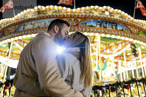 Paar küsst sich vor Karussell auf dem Weihnachtsmarkt