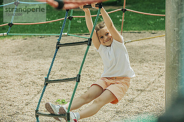 Lächelndes Mädchen klettert Strickleiter auf Spielplatz