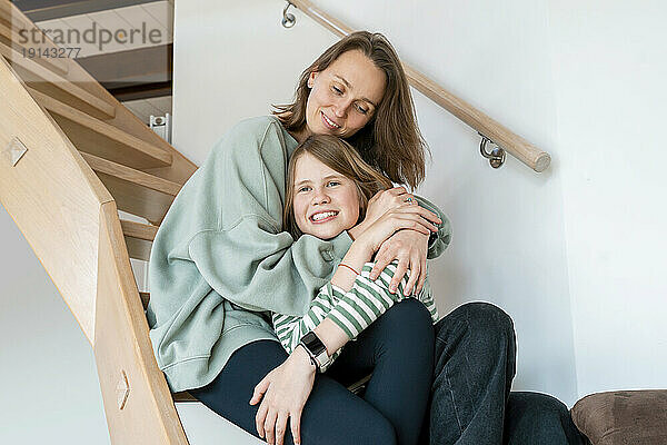 Mother embracing daughter sitting on steps at home