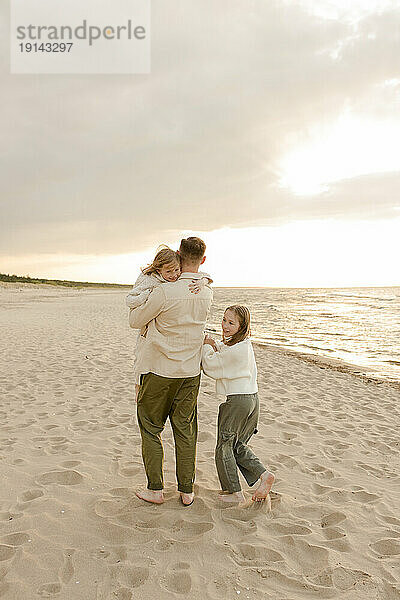 Glückliche Töchter mit Vater  die am Strand spazieren gehen