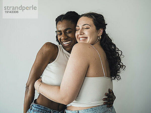 Happy young women with eyes closed in front of wall