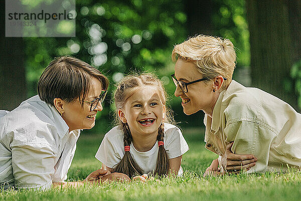 Happy lesbian couple with daughter lying on grass at park
