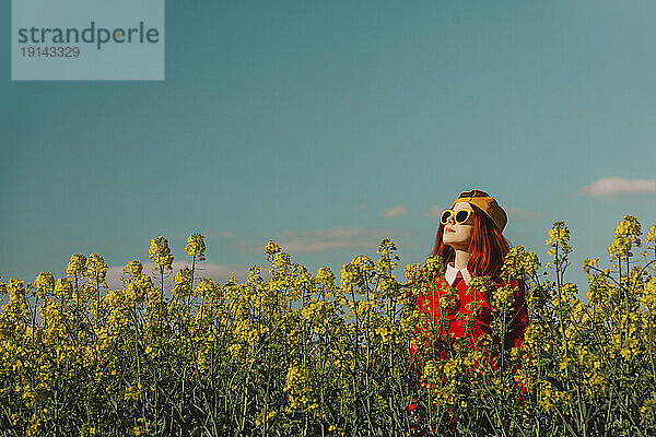 Frau mit Sonnenbrille steht an einem sonnigen Tag im Rapsfeld