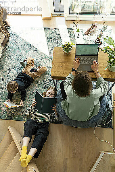 Freiberufler arbeitet am Laptop und Kinder lesen zu Hause ein Buch