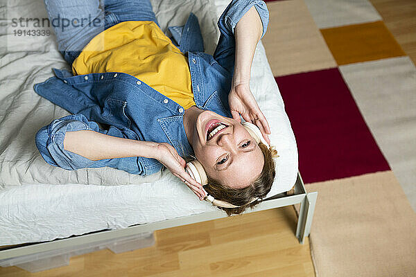 Cheerful woman enjoying music with headphones lying on bed