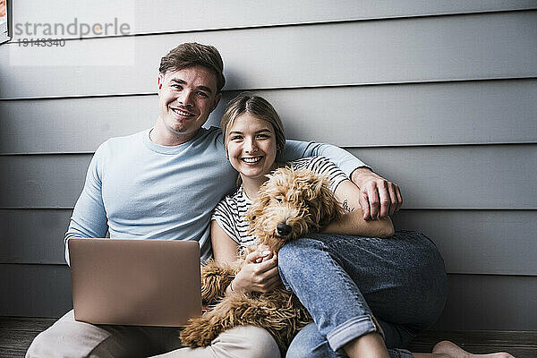 Glückliches junges Paar sitzt mit Hund vor der Wand
