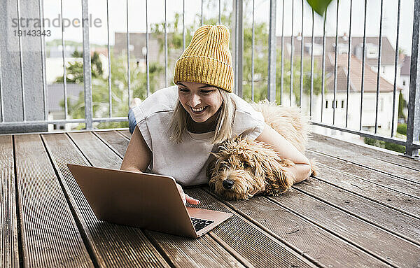 Glückliche junge Frau benutzt Laptop auf dem Balkon
