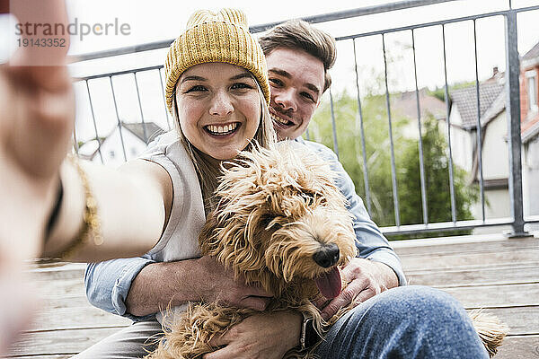 Glückliche Frau macht Selfie mit Mann und Hund auf dem Balkon