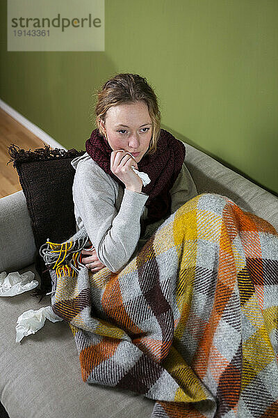 Kranke junge Frau  in eine Decke gehüllt  entspannt sich auf der Couch