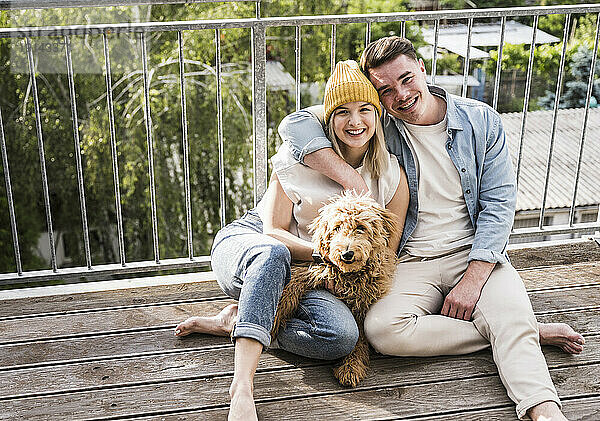 Happy young man and woman sitting with dog on balcony