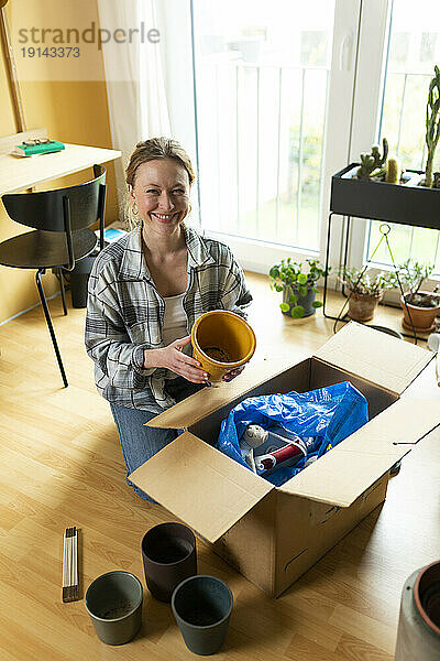 Lächelnde Frau hält Behälter neben Karton zu Hause