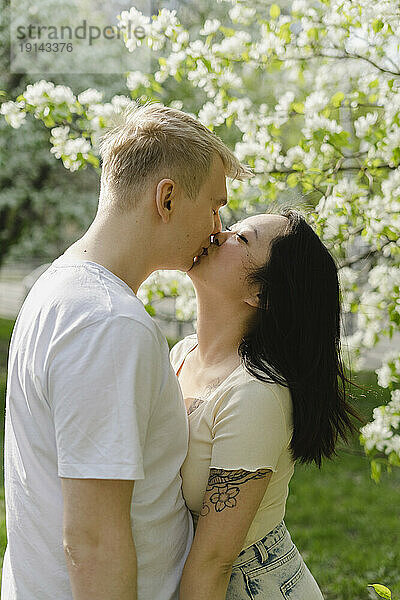 Junges Paar küsst sich am blühenden Baum im Park