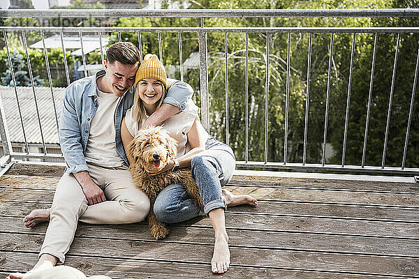 Liebevolles junges Paar sitzt mit Hund auf dem Balkon