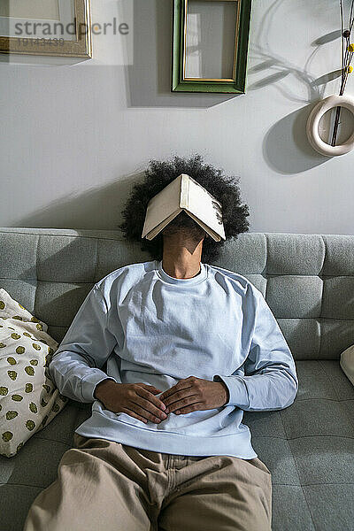 Müder Mann schläft zu Hause auf dem Sofa mit Buch im Gesicht