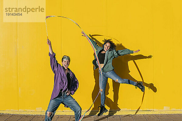 Fröhliches lesbisches Paar  das sich an einem sonnigen Tag vor der gelben Wand amüsiert