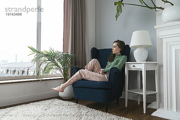 Nachdenkliche junge Frau entspannt sich zu Hause im Sessel