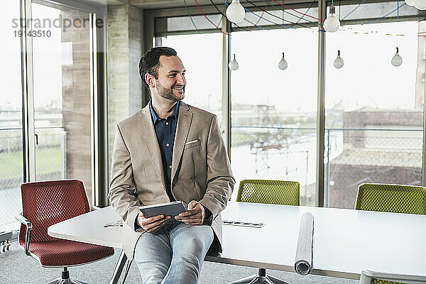 Lächelnder Geschäftsmann mit Tablet-PC sitzt am Tisch im Büro