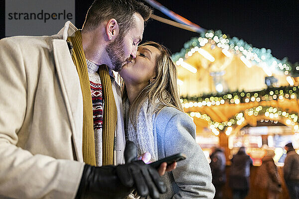 Junge Frau küsst Mann auf Weihnachtsmarkt