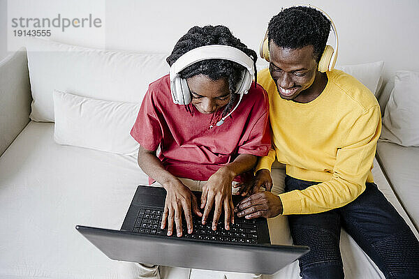 Lächelnde junge Freunde  die sich zu Hause auf der Couch einen Laptop teilen