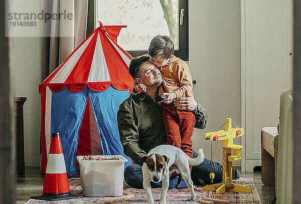 Son kissing father sitting near by dog at home