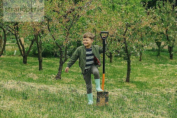 Smiling boy with shovel standing in front of trees at garden