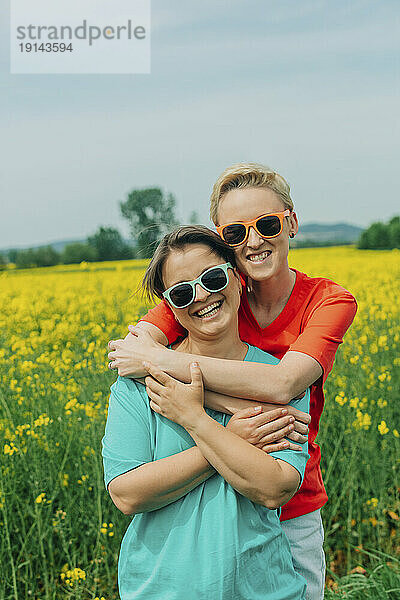 Fröhliche Lesben mit Sonnenbrille umarmen sich und stehen auf dem Feld