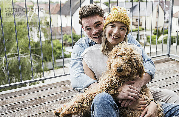 Glückliches Paar sitzt mit Hund auf dem Balkon