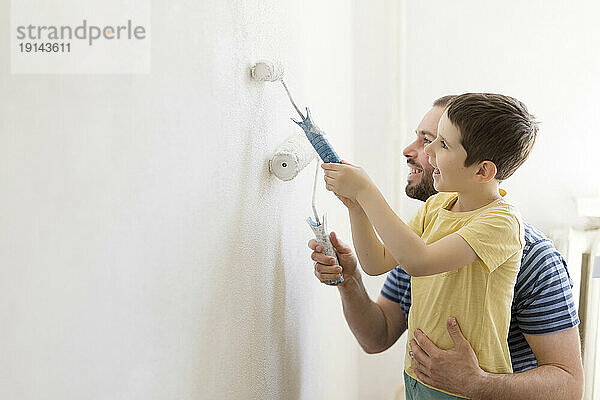 Lächelnder Vater und Sohn malen Wand zu Hause