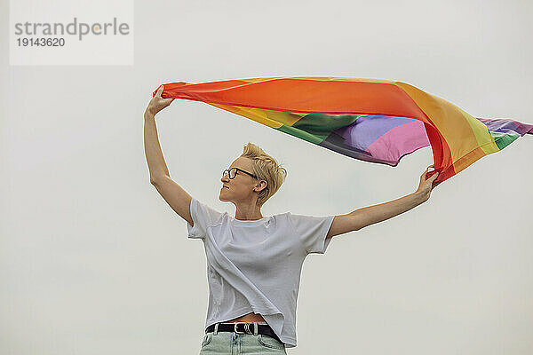 Glückliche Frau hält Regenbogenfahne vor dem Himmel