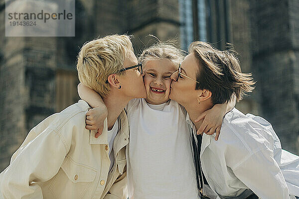Glückliche Tochter  die an einem sonnigen Tag von einem lesbischen Paar geküsst wird