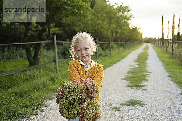 Smiling girl holding Hydrangea flower standing on footpath