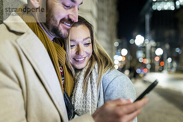 Glückliche junge Frau mit Mann  der Smartphone benutzt