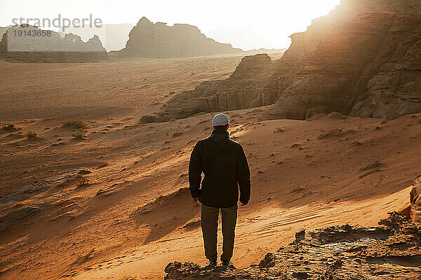Mann steht bei Sonnenaufgang auf einem Felsen in der Wüste