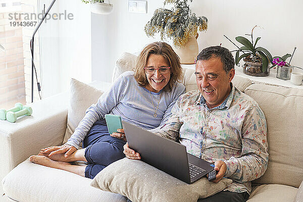 Mann teilt Laptop mit glücklicher Seniorin  die zu Hause auf dem Sofa sitzt