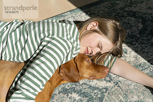 Mädchen liegt an einem sonnigen Tag mit Hund zu Hause auf dem Teppich