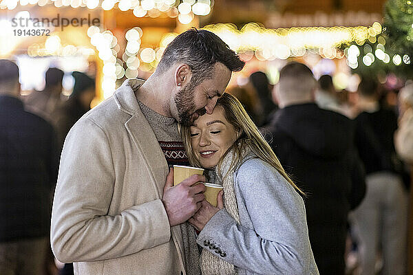 Liebespaar umarmt sich mit einer Kaffeetasse auf dem Weihnachtsmarkt